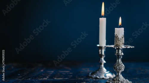 An ornate silver candlestick holder with a white taper candle, set against a background of dark midnight blue photo