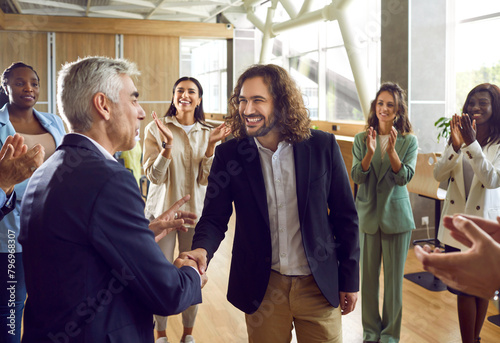 Nice work, young man. Diverse business team celebrating colleague's successful job promotion and having fun together. Smiling boss exchanges handshakes with happy employee while others clap hands