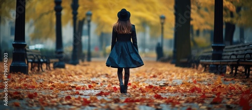A woman walks through a park with scattered autumn leaves