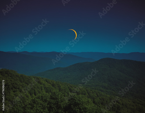 Thin Crescent Moon in a Starry Night Sky Over a Forested Landscape
