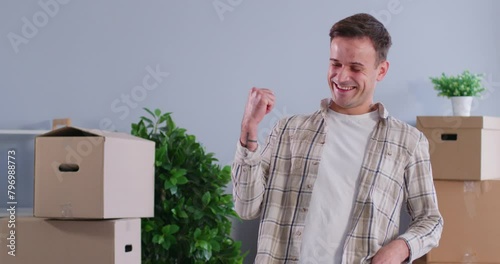 Man moving to new house or apartment. Happy, joyful homeowner, standing in room full of boxes, smiles, shows key, tosses it from one hand to other, and says Yes, I did it. Buying property concept photo