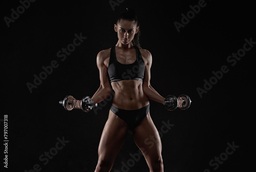 Sporty brunette woman in sports underwear posing in studio with dumbbells