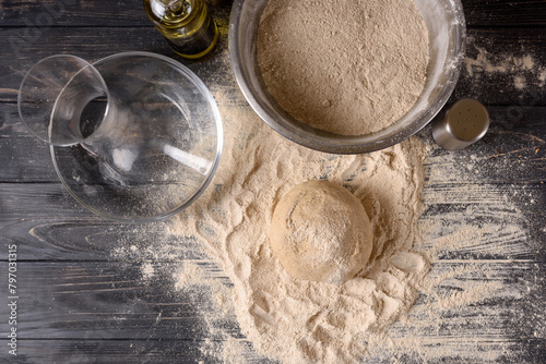 Top view of ingredients for making dough in the kitchen. Kneading dough for baking baked goods or pizza. Water, flour are scattered on the table, oil and salt are on a dark wooden table. Flatley shot.