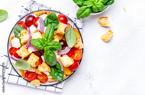 Fresh summer salad with tomatoes, stale bread, onion, cheese, green basil and olive oil, white table background, top view photo