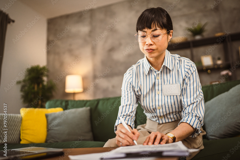 Mature japanese woman with eyeglasses work from home and sign document Mature japanese woman with eyeglasses work from home and sign document
