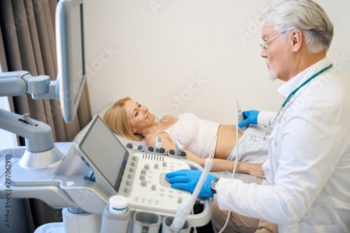 Mature man using ultrasound scan examining woman in modern hospital