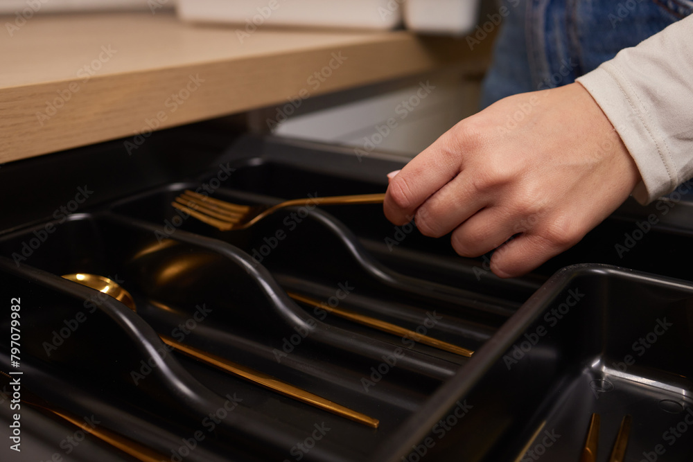 Person grabbing gold fork from black drawer with handles Person grabbing gold fork from black drawer with handles
