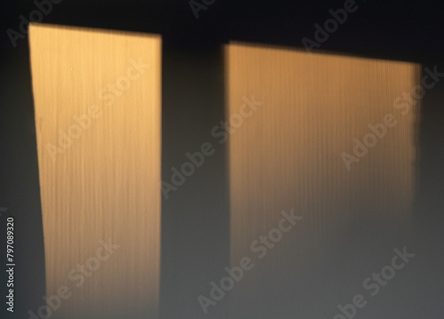 Soft warm evening sunlight through the window shinning onto dark interior wall creates a cozy ambience. Abstract gold colored background. 