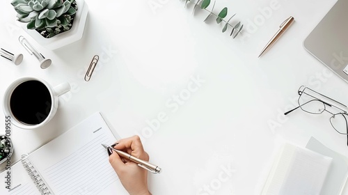 Simple white desktop with one hand writing on a piece of paper with a neutral pen and some note-taking tools on the table photo