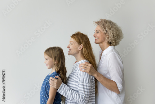 Little girl her young adult mummy and mature grandma posing on gray studio wall background, showing unity, deep-rooted connections, shared history among family members across different stages of life