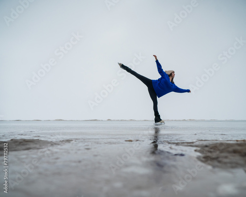 Caucasian woman in a blue sweater is skating on a frozen lake. Figure skater performs a swallow. 