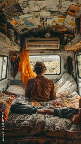 A man sits on a bed in the back of a van  looking out the window.