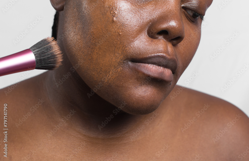 Brown skinned woman applying foundation with makeup brush, dark skin