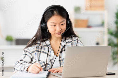 Concentrated young chinese woman taking notes from an online video at home