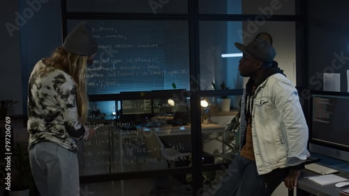 Medium full of African American male and Caucasian female programmers brainstorming ideas for software project in IT startup office, writing code on glass wall in white marker, discussing problems photo