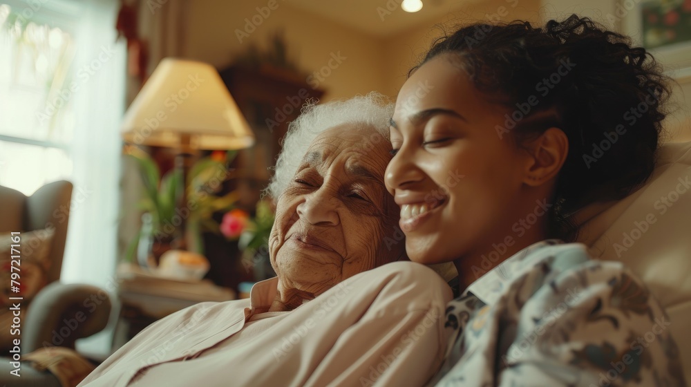 An elderly woman and a young woman are sitting on a couch and smiling at each other. An elderly woman and a young woman are sitting on a couch and smiling at each other.