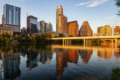 In Austin, Texas, at Lady Bird Lake, the modern city casts golden reflections during the golden hour. Viewed from the shoreline park on a warm summer evening, it's a breathtaking sight.