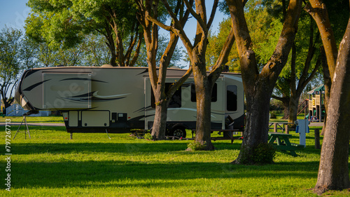 Camping in Rv fifth wheel trailer under trees on grass 