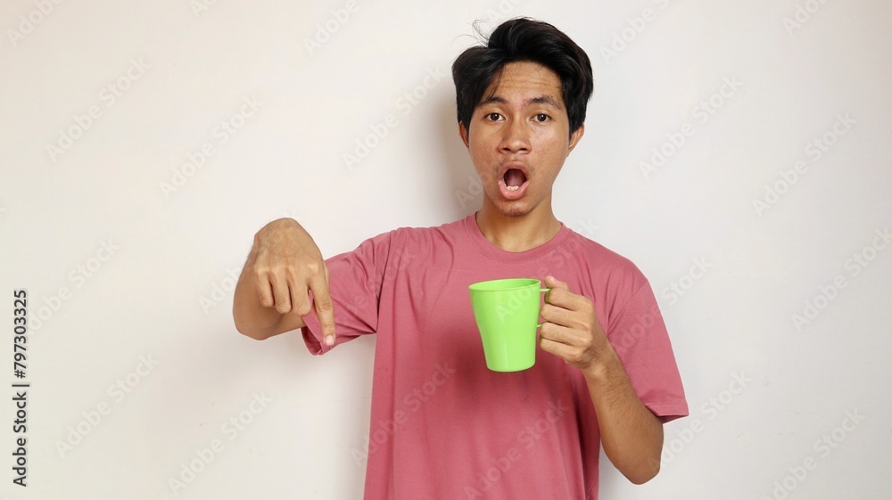 young shocked asian man posing pointing to the bottom side holding a cup on an isolated white background young shocked asian man posing pointing to the bottom side holding a cup on an isolated white background