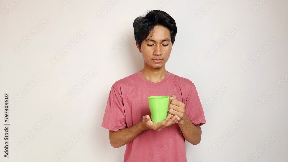 young asian man posing holding and looking at a cup on an isolated white background. young asian man posing holding and looking at a cup on an isolated white background.