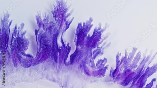 Purple and pink swirls in an acrylic pour painting create intricate patterns on a white background. The fluidity of the liquid paint creates delicate lines that resemble fractal structures. photo