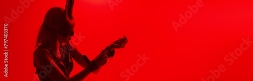 sexy submissive woman slave girl in mask and BDSM handcuffs on a red background. Wide horizontal banner header with a copy space