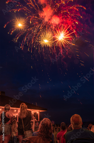 Fourth of July fireworks in small Midwestern town; figures of people sitting and standing in foreground; lit gazebo in background