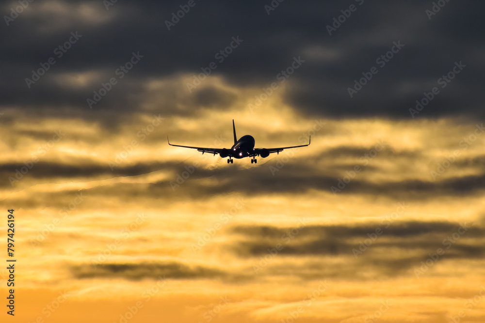 commercial airplane coming in for a landing at dusk, with dramatic sky in the background.