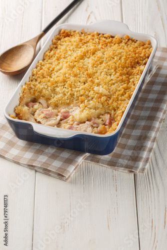 Chicken Cordon Bleu Casserole with chicken breast, cheese and ham melted in cream closeup in the baking dish on the white wooden table. Vertical
