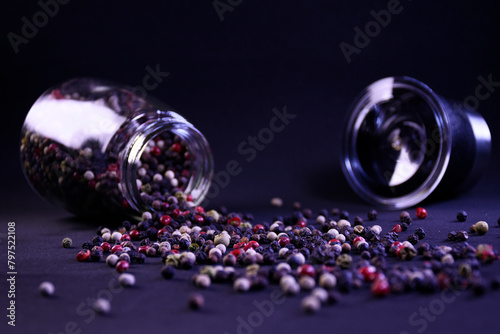 peppercorns scattered from a pepper shaker on the surface on a black background to add flavor and aroma to dishes photo