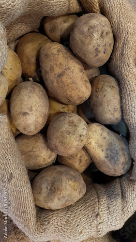 Top view of unwashed potatoes yams, heaps of fresh organic raw potatoes in the sack for sale at market, whole food nature concept, organic