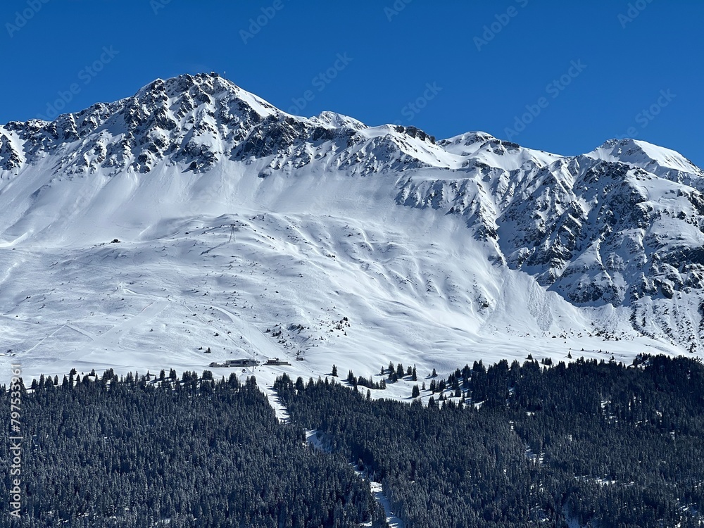 Obraz premium Beautiful sunlight and snow-capped alpine peaks above the Swiss tourist sports-recreational winter resorts of Valbella and Lenzerheide in the Swiss Alps - Canton of Grisons, Switzerland (Schweiz)