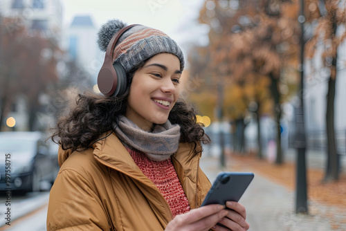 Happy young woman holding mobile phone enjoying music listening through wireless headphones on footpath  © Fabio