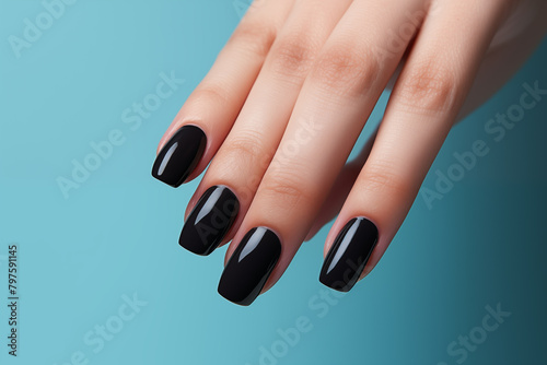 Glamour woman hand with luxury black color nail polish on her fingernails. Hand with black nail manicure with gel polish on blue background. Nail art and design. Female hand model. French manicure.