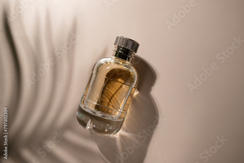 Golden perfume with leaf shadow on beige background, elegant bottle with transparent packaging, luxury fragrance for the modern woman