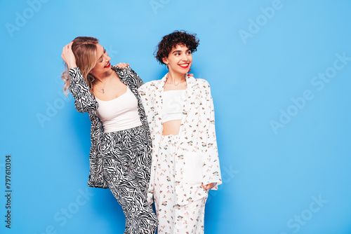 Two young beautiful smiling brunette hipster female in trendy summer costume clothes. Sexy women posing near blue wall in studio. Positive models having fun. Cheerful and happy. Going crazy