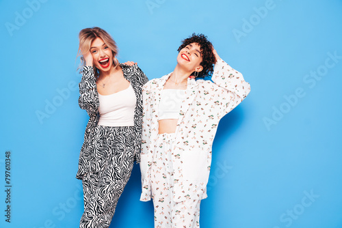 Two young beautiful smiling brunette hipster female in trendy summer costume clothes. Sexy women posing near blue wall in studio. Positive models having fun. Cheerful and happy. Going crazy