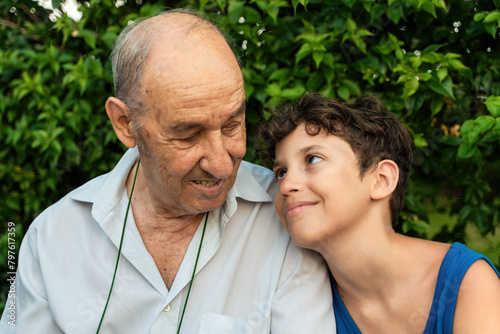 Grandfather and grandson enjoying a shared laugh in a serene garden - Elderly man and a young boy gazing in a tender moment, surrounded by lush greenery - intergenerational bonds.