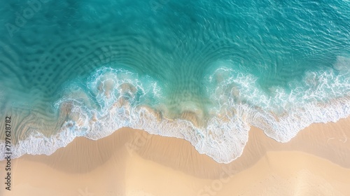 A sandy beach with gentle waves rolling onto the shore in an aerial view of the ocean