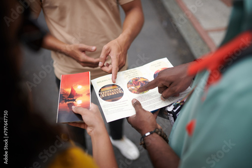 Hands of young male traveler and guide pointing at brochure template during excursion while discussing famous sights of the city © pressmaster