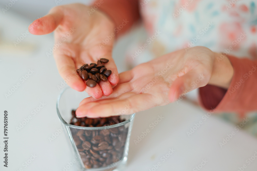 Obraz premium Close-up of girl's hands showing roasted coffee bean with blurred background behind. Shallow depth of field focused on coffee bean. Concept of individual approach to quality control.