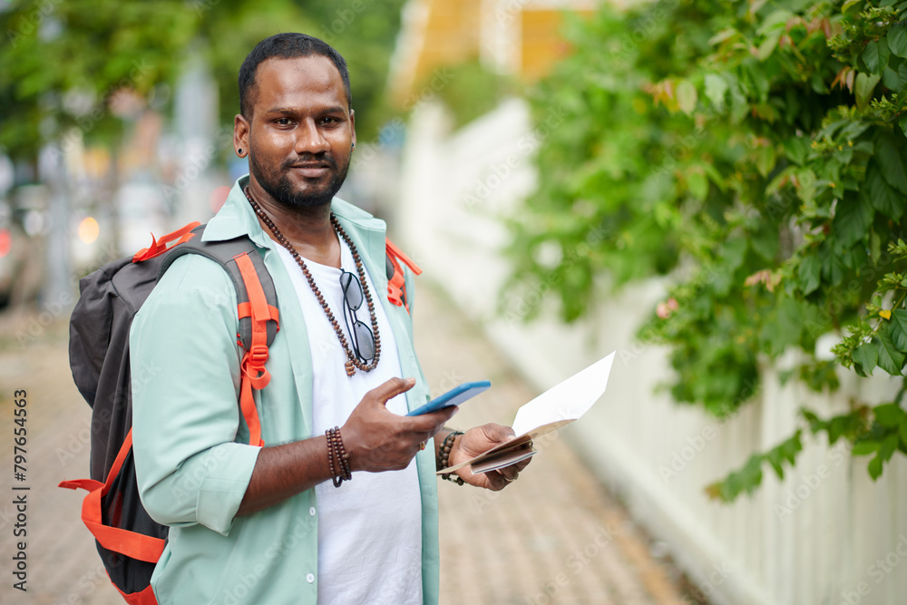 Guy in casualwear looking at camera and using mobile phone while enjoying sightseeing excursion during summer vacation Guy in casualwear looking at camera and using mobile phone while enjoying sightseeing excursion during summer vacation