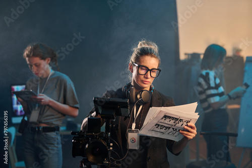 Waist up portrait of adult woman as female director looking at scene cards while leading video production on set copy space