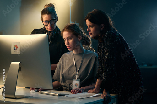 Minimal shot of three women looking at computer screen together on video production set with backlight