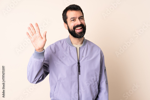 Caucasian man with beard wearing a jacket over isolated background saluting with hand with happy expression