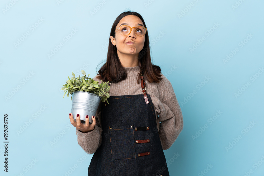 Φωτογραφία Young brunette mixed race woman holding a plant over isolated blue background and looking up