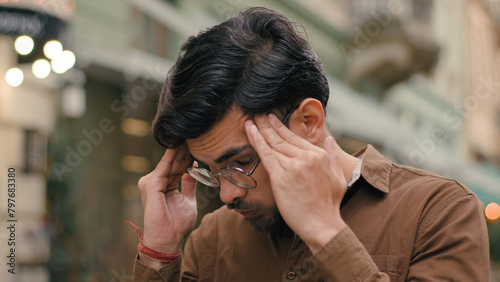 Annoyed angry mad stressed Indian Arabian ethnic male student man guy businessman client customer furious business fail loss dissatisfaction frustration headache touch holding head outside city street