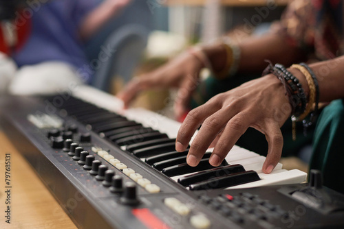 Hand of young unrecognizable male musician pressing keys of electronic synthesizer while composing, performing and recording his music