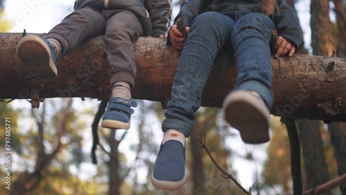 children sitting on a tree in the park. happy family childhood dream concept. children dangle their legs while sitting resting on a fallen tree trunk in the forest in lifestyle the park