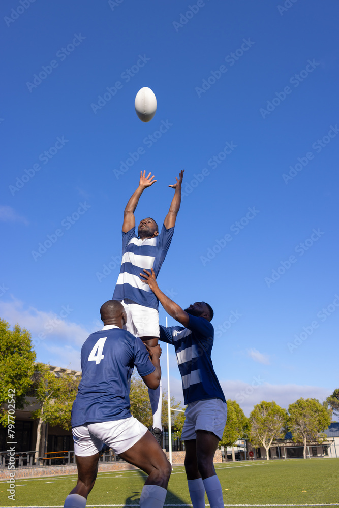 Obraz premium Three young African American men play rugby, one leaps for the ball